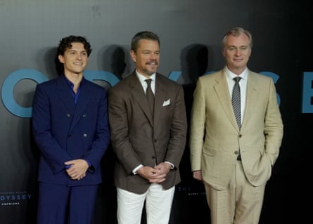 three men in suits stand on red carpet smiling