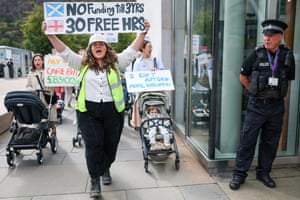 A protester in a hi-vis vest holds up a home-made sign comparing Scottish and English childcare provision