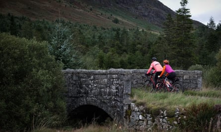 Brightly dressed cyclists riding over stone bridge in hilly scenery