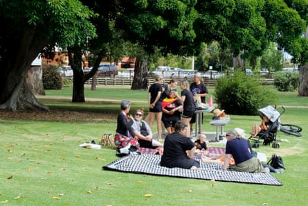 Children and adults sit on picnic rugs in the park