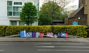 A row of estate agent boards lying on their sides next to a hedge