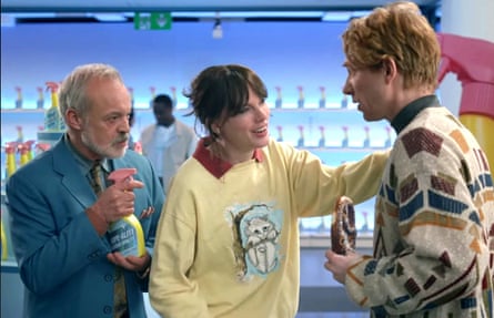 A woman with a yell0w sweatshirt, a man in a blue suit, and a red-haired man in a patterned jumper