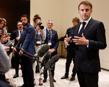 Emmanuel Macron gestures while speaking to journalists holding microphones and cameras