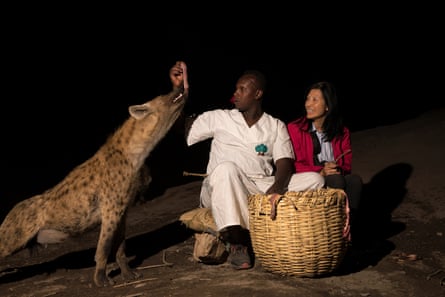 A tourist looks on as a hyena takes a piece of meat from Abbas’s hands.