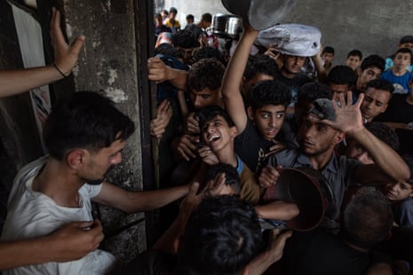 Hundreds of internally displaced Palestinian people gather outside a charity kitchen in Gaza city to receive limited food rations.