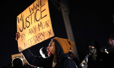 A man chants while holding a sign that reads 'We want justice by any means necessary'.