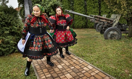 Women dressed in traditional costumes pass a war memorial on their way to the village wedding hall