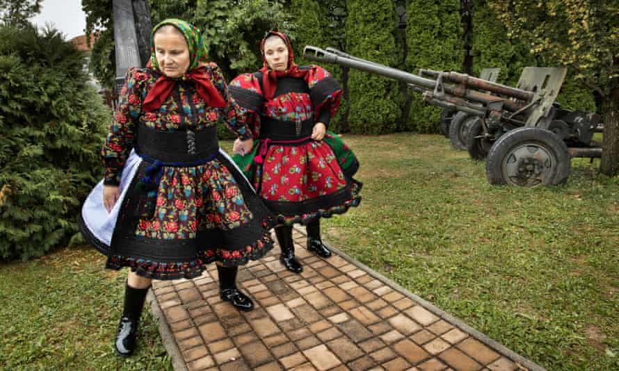 Women in traditional costumes pass a war memorial on their way to the village wedding hall