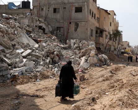 A woman walks along a devastated street in the West Bank