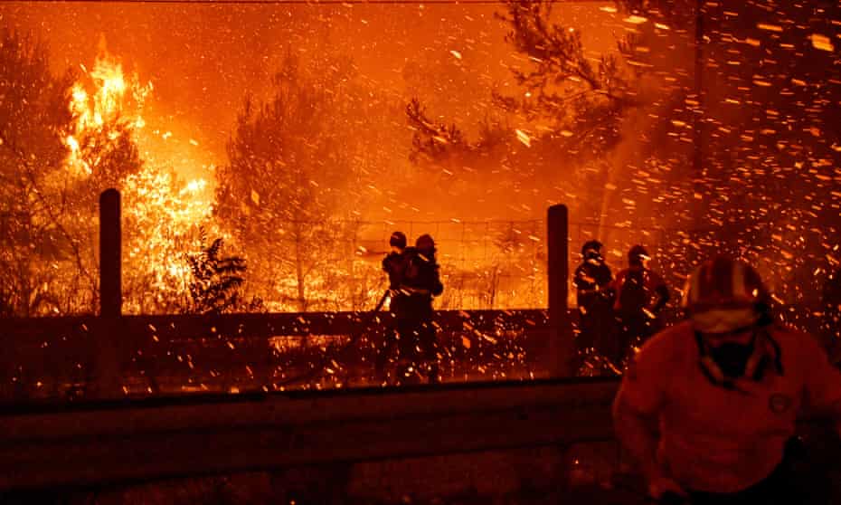 Firefighters try to put out a fire as flames spread over a highway during a wildfire in northern Athens, Greece