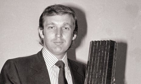 Black-and-white image of young white man with slicked-back hair, in suit, holding tall metal object.