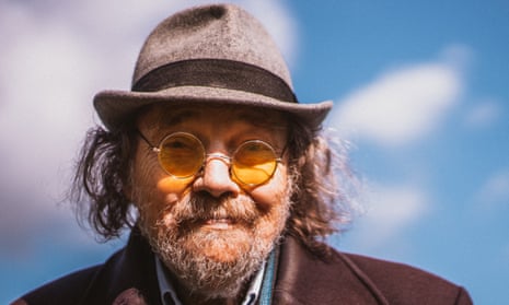 Bill Fay, with a beard, in an overcoat, trilby hat and round glasses, smiling slightly in the sun