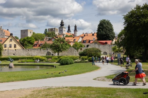 The medieval walls of Visby are seen in the background as people go for a walk around a park