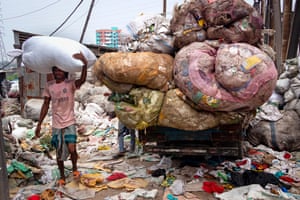 A man carrying a huge plastic sack on his head, and surrounded by plastic rubbish