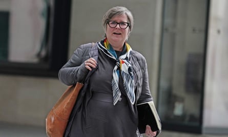 Saffron Cordery, wearing grey dress with colourful scarf around her neck and carrying a light brown bag