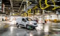 Deliberately blurry image of a small modern white van veing driven through a large factory