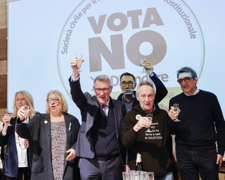 People hold up glasses of sparkling wine in front of a backdrop with the words 'Vota No'
