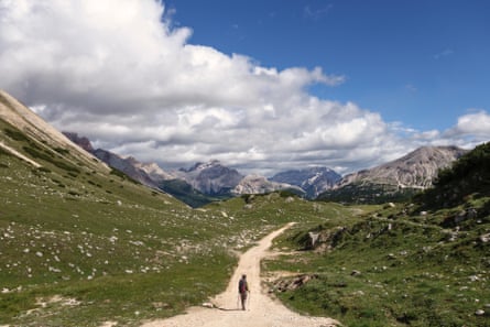 A one hiker walking on a path in a grassy valley with mountains in the distance