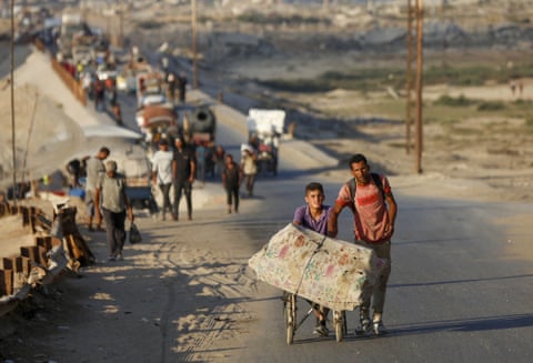مردم در امتداد جاده آسفالت قدم میزنند - پسری در کنار مردی تشکی را روی ویلچر هل میدهد،