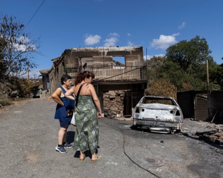 Local women watch as car and properties are burned along the street on August 20, 2025 in Caridade, Ourense province, Spain.