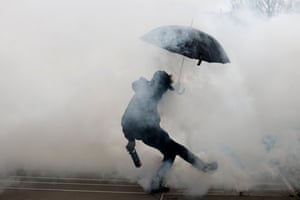 A protester shields himself with an umbrella as he kicks a teargas canister during clashes with police in Nantes