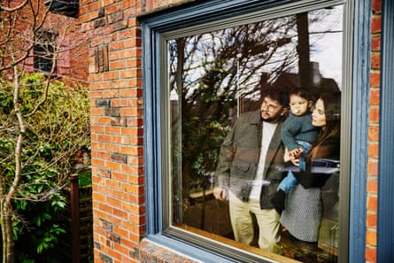 Attractive couple with baby peer out through a large window