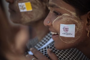 A woman wears a sticker showing the face of Pope Francis as she and a relative listen to a mass led by the pope at St. Mary’s Cathedral in Yangon