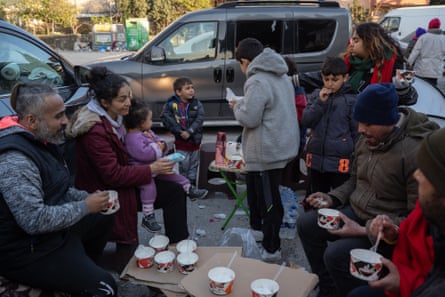 People gathered round a table with pots of food in the street