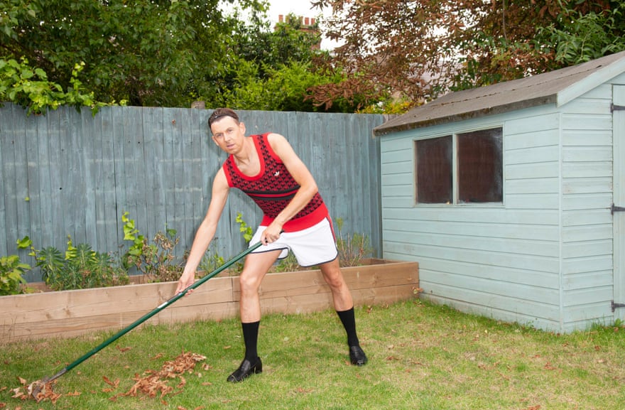 Tim Jonze raking leaves in the garden wearing a patterned red tank top, white shorts, black socks and loafters