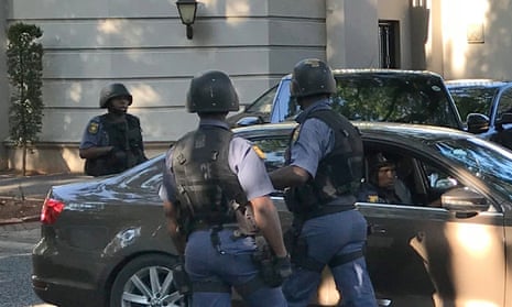 Three members of the Hawks South African police unit standing around a car in helmets and bulletproof vests