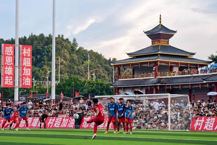 Footballers play in a match on a field in front of a pagoda