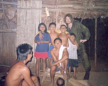 Bushby in combat fatigues, posing with two adults and five children in a grass-roofed hut