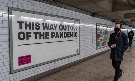 A man in a mask walking past a billboard that says 'This way out of the pandemic', referring to mass global vaccination