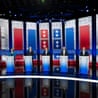 Seven California governor candidates stand behind podiums on a debate stage with red, white, and blue decorations