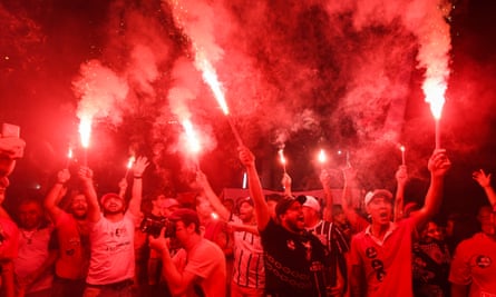 Supporters of Brazilian President-elect Luiz Inacio Lula da Silva celebrate his victory in São Paulo. [Picture of a crowd of people in Brazil lighting flares that turn the air above them red and cause smoke]
