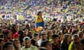 A sad-looking woman wrapped in a Colombian flag perched on someone's shoulders amid a subdued crowd