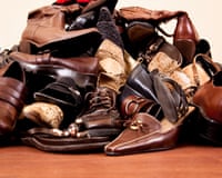 A large jumbled pile of brown and black leather shoes, boots, and sandals sits on a wooden floor
