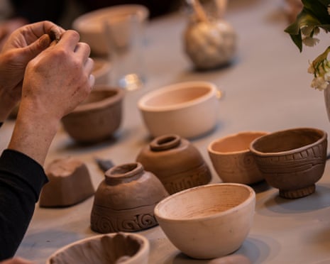 A pair of hands shape a piece of clay while various small pots sit on a table in front of them.