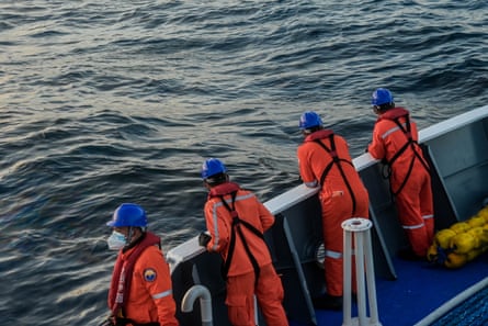Four coast guards in orange look for signs of oil from a ship