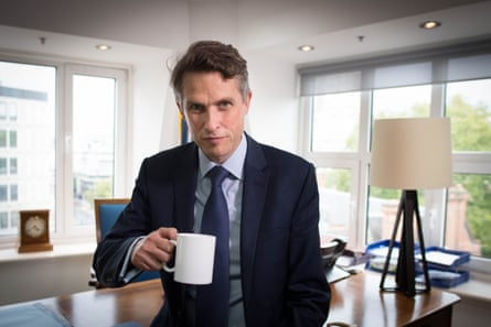 A man sits on an office desk holding a white mug.