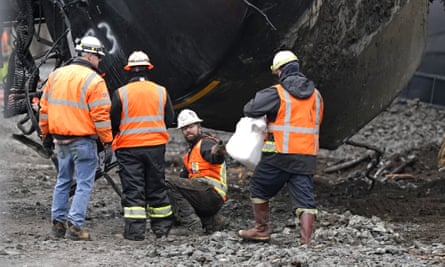 A worker reaches for absorbent pads as residual oil leaks from a train car being readied to be moved following a derailment, December 2020.