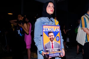 A woman holds a poster with an image of a man that reads ‘Zohran’