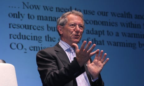 Sir David King giving a presentation on stage ina a shirt and jacket, with a display of highly magnified text on a screen behind him
