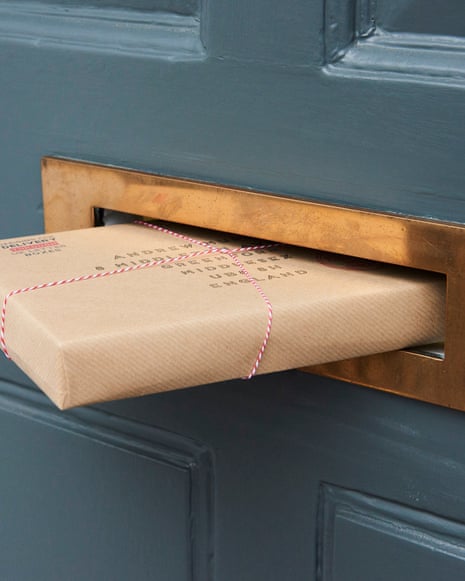 brown paper parcel halfway through a gold letterbox in a dark grey door.