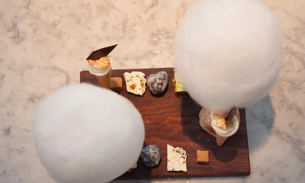 Two large circles of candyfloss on a wooden board with a variety of other smaller desserts