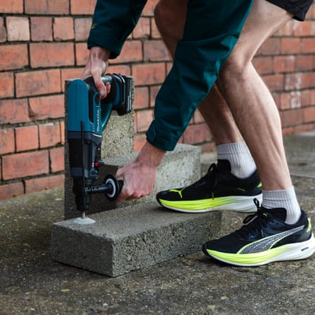 The writers legs are in view and he is wearing sports shoes socks and shorts. The Marika Brushless Combi drill is being used by the writer to drill down into a concrete slab.