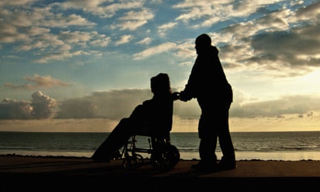 Silhouetted man pushing a person in a wheelchair along a seafront at sunset