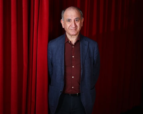 a man in a suit stands next to a red curtain