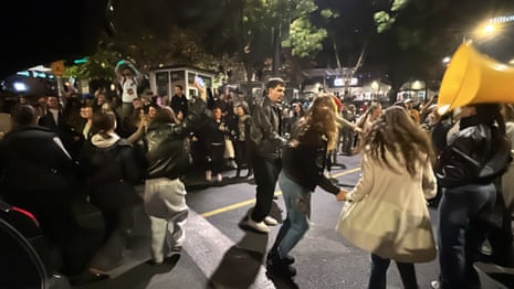 People in Belgrade dance and hold hands in a circle on a street at night