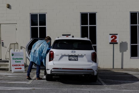 A Parkside Pediatrics provider in protective gown examines a patient inside a parked SUV